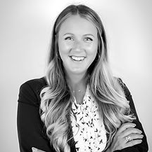 Smiling woman with blonde hair, arms crossed, wearing a blazer and patterned top.