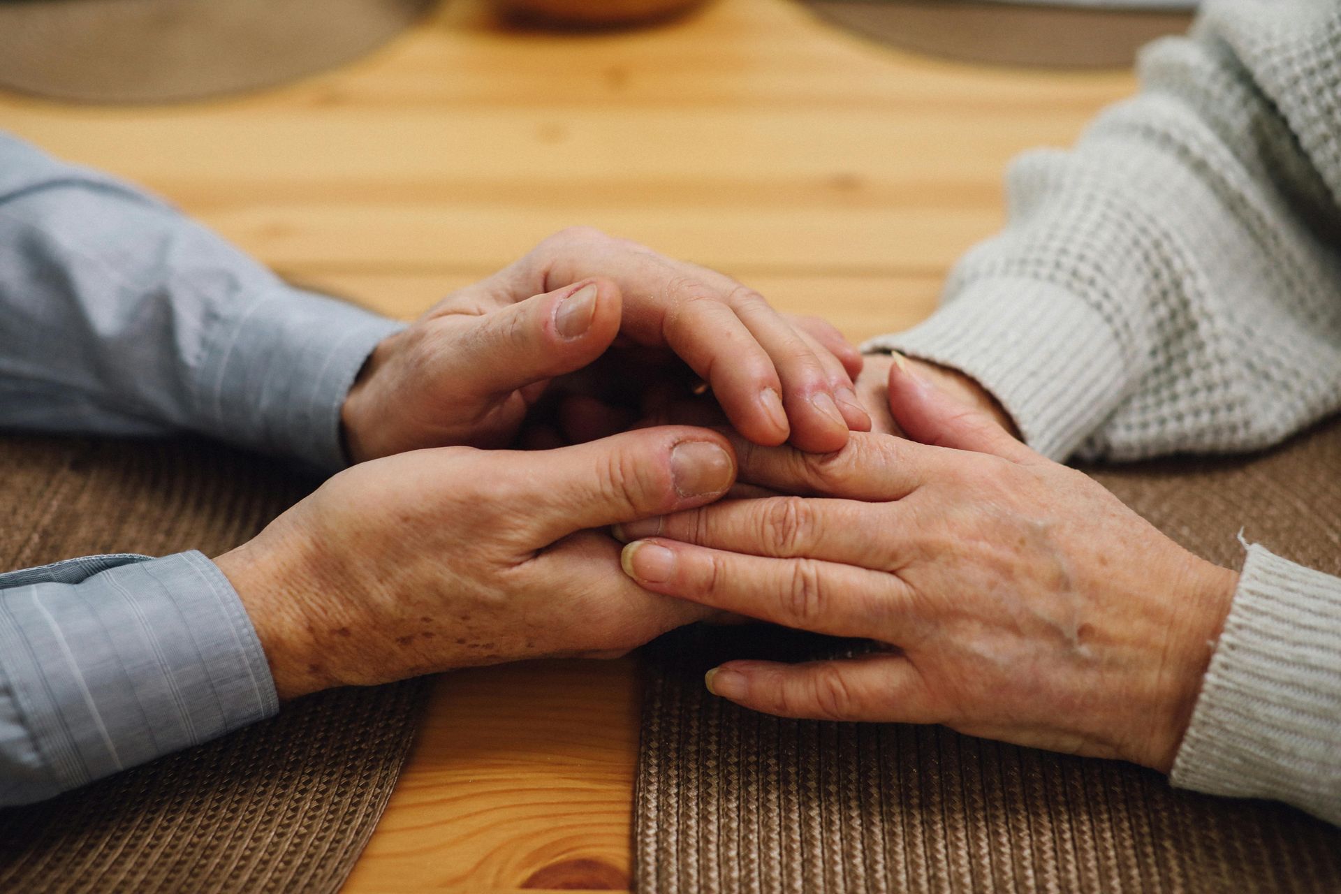Two people holding hands on a wooden table, offering comfort and support.