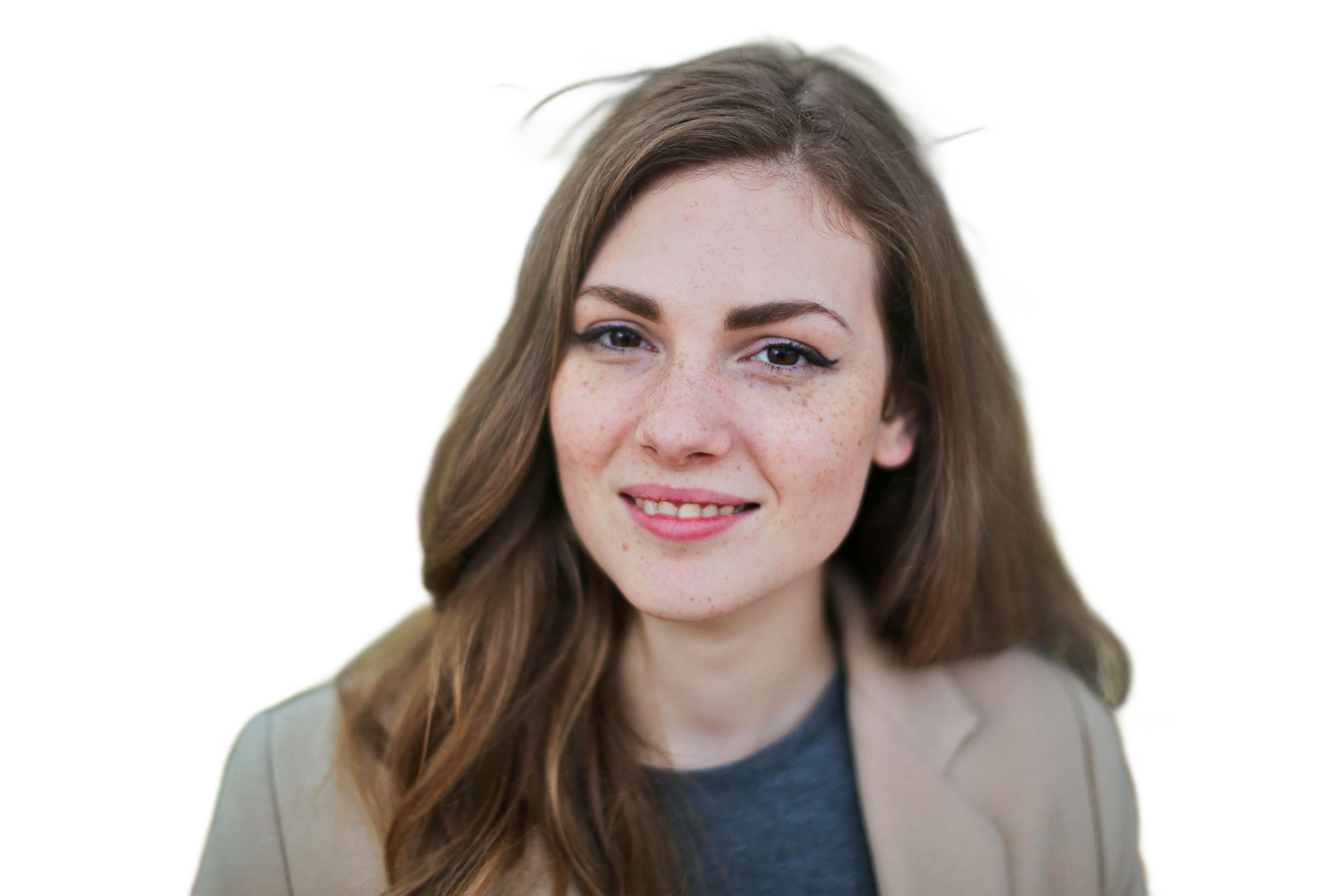 Woman with freckles smiles, wearing a beige blazer and gray shirt, with long brown hair.