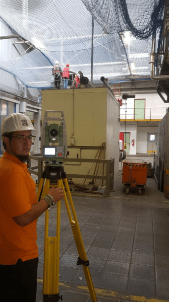 Ein Mann in einem orangefarbenen Hemd steht vor einer Kamera auf einem Stativ.