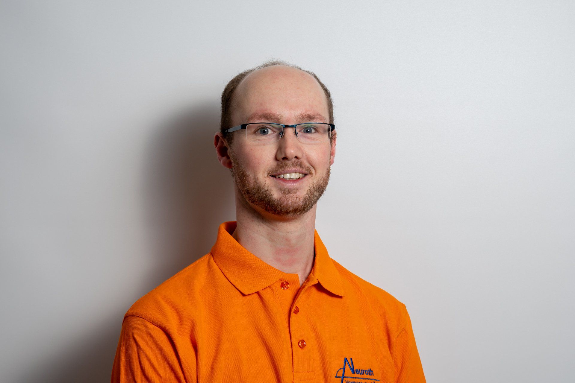 Ein Mann mit Brille und orangefarbenem Hemd lächelt in die Kamera.