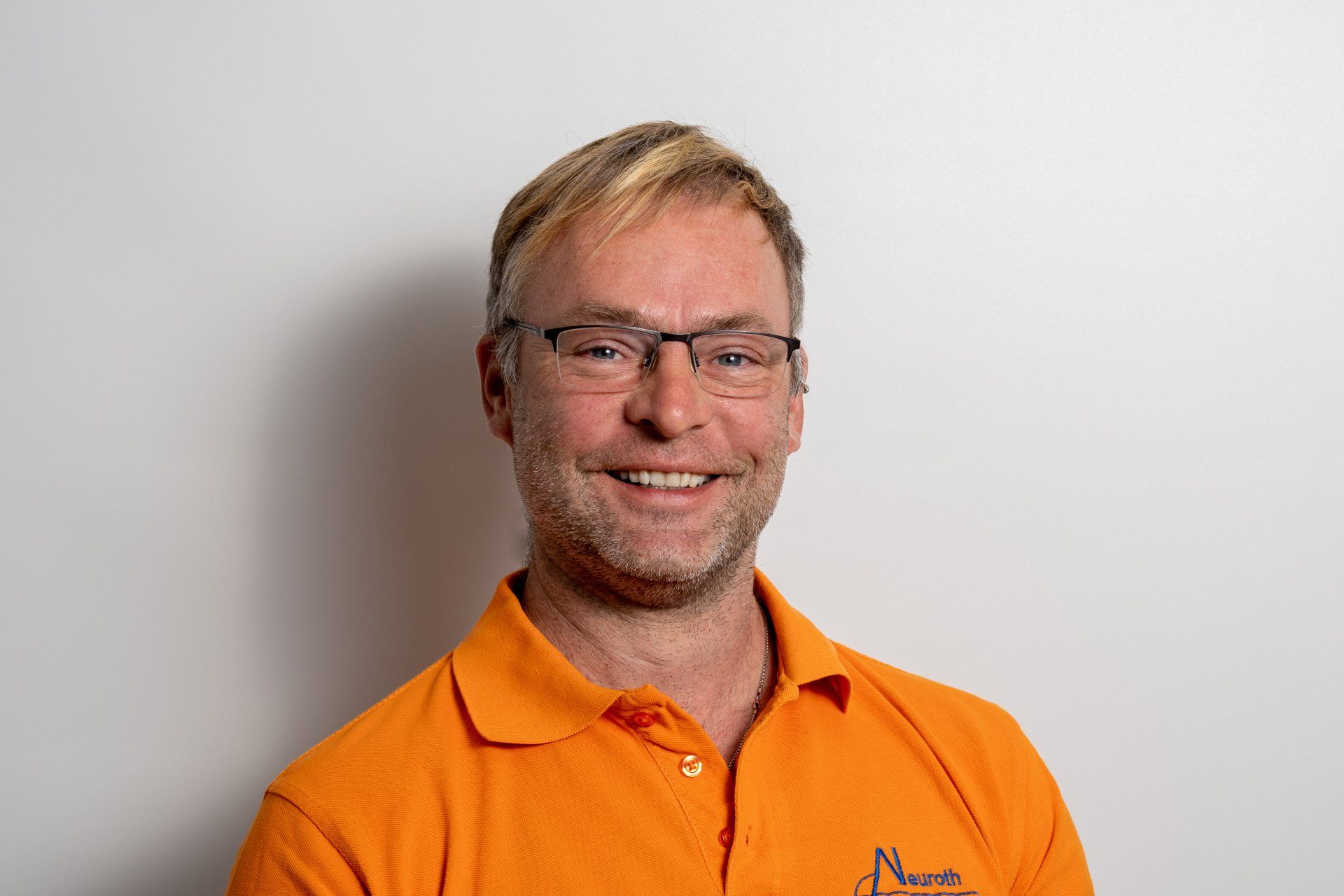 Ein Mann mit Brille und orangefarbenem Hemd lächelt in die Kamera.