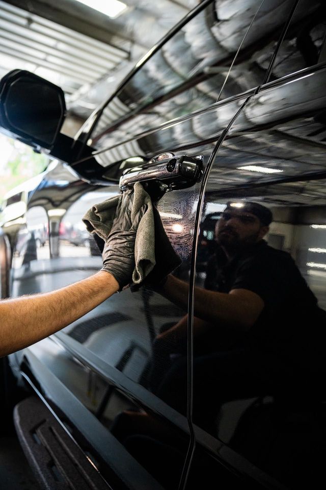 A man is cleaning the wheel of a black car with a sponge.