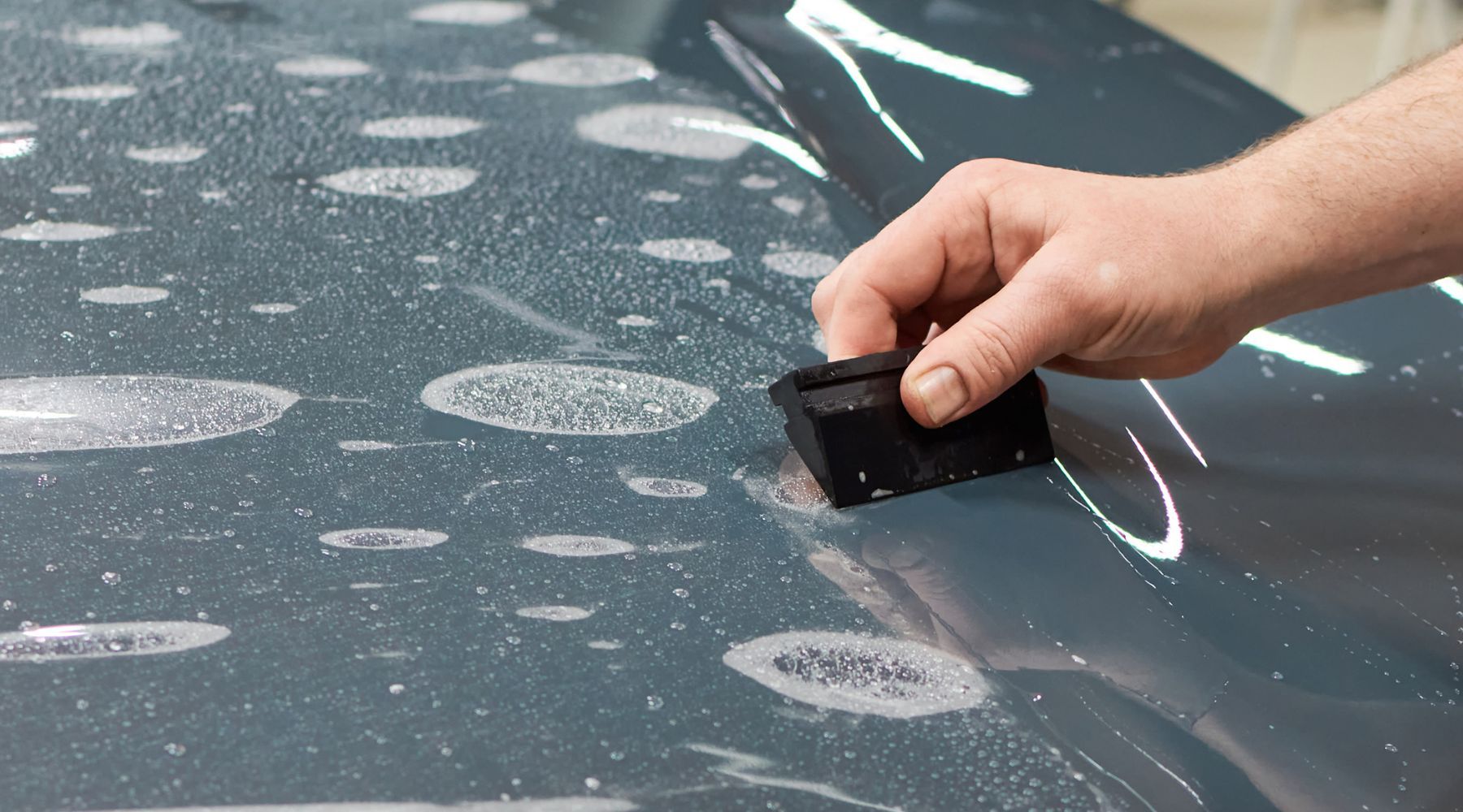 A person applying paint protection film (PPF) on a car's surface using a squeegee, with water bubble