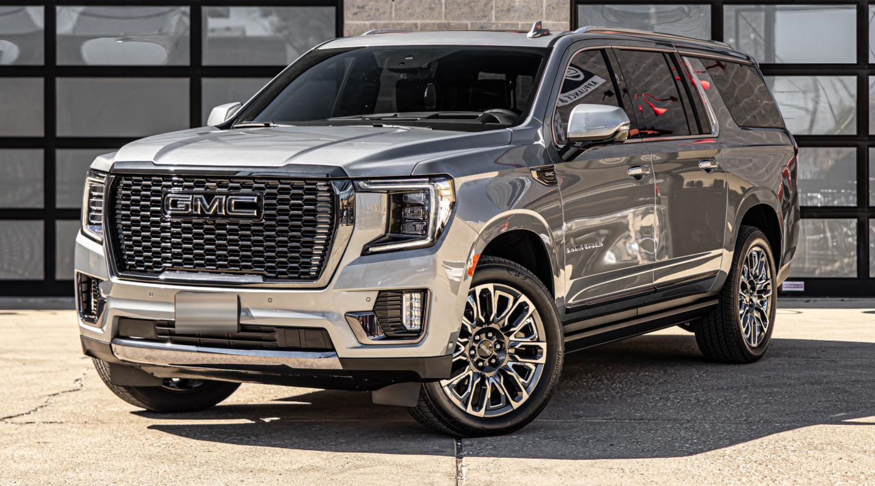 The image shows a large, silver GMC SUV with black, glass-paneled doors parked in front of a garage.