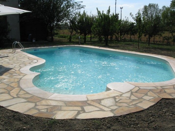 Piscina con acqua azzurra, bordo in pietra e paesaggio circostante.