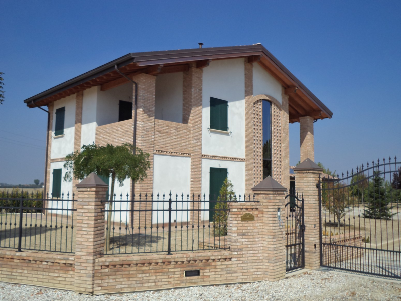 Casa a due piani in mattoni bianchi con ingresso recintato in una giornata di sole.