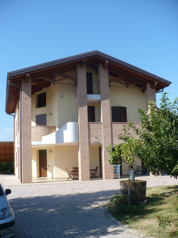 Casa beige a due piani con colonne in mattoni, tetto marrone e vialetto d'accesso in una giornata di sole.