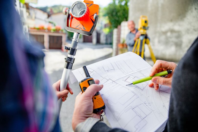 Due topografi pianificano utilizzando una mappa e un walkie-talkie; l'attrezzatura sullo sfondo.