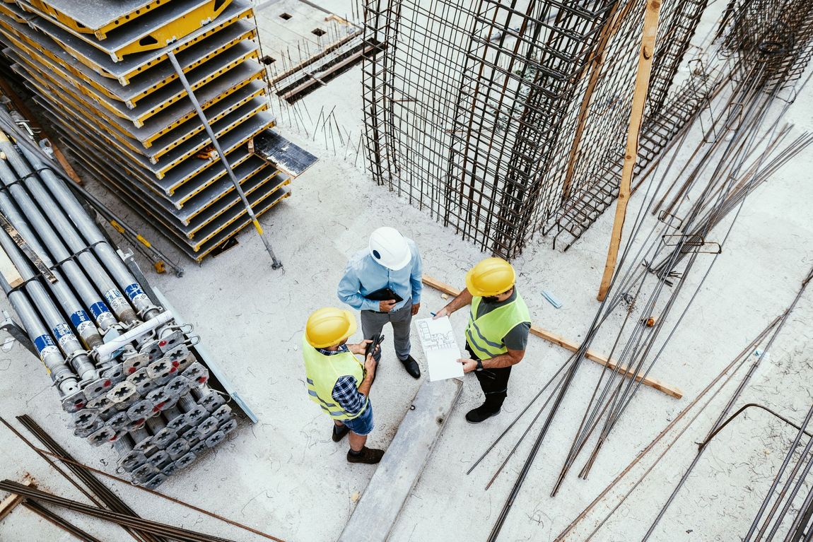 Gli operai edili con i caschi gialli esaminano i progetti in un cantiere con cemento e acciaio.