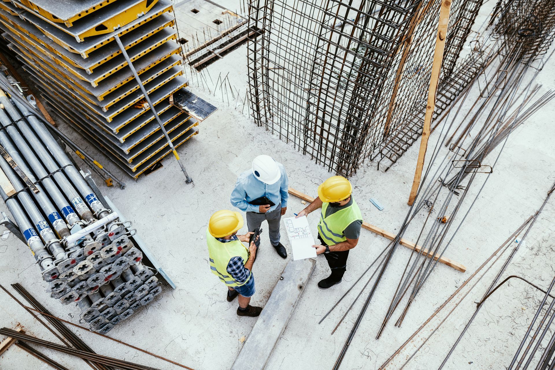 Gli operai edili con i caschi gialli esaminano i progetti in un cantiere con cemento e acciaio.