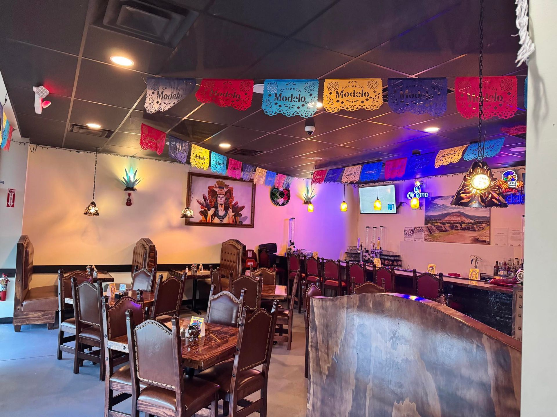 A restaurant dining area featuring wooden chairs and tables, decorated with colorful papel picado banners on the ceiling.