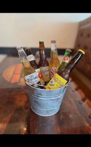 A galvanized metal bucket filled with assorted glass beer bottles sits on a dark wooden table.