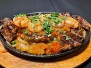 A sizzling skillet of grilled steak and shrimp topped with fresh cilantro, served over a bed of onions and peppers.