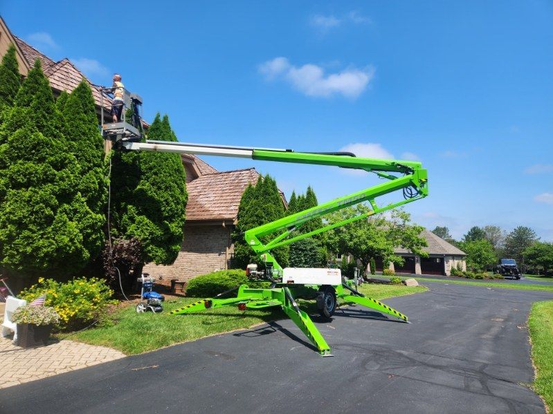 Bright green boom lift beside a stone building and hedge on a sunny street