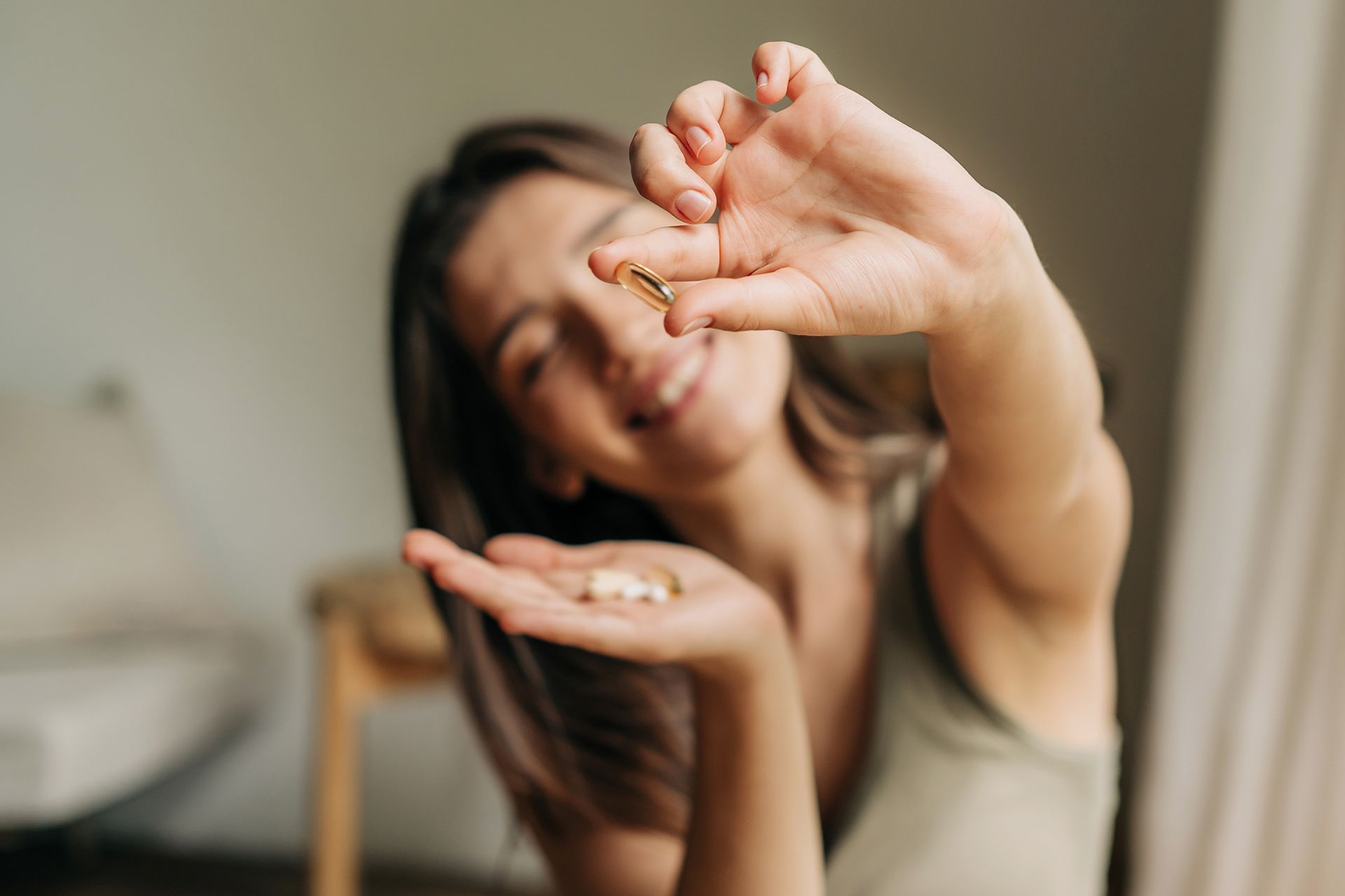 Woman holding out pills, smiling. Light-skinned, wearing green top, natural lighting.