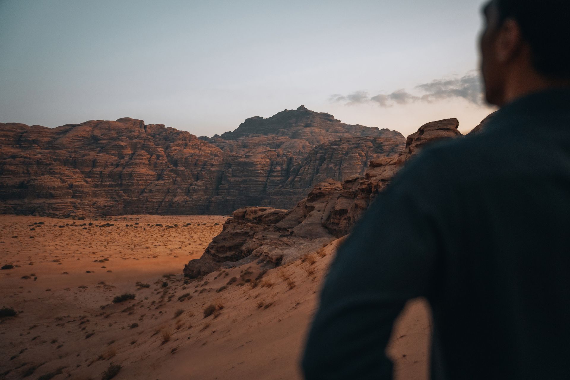 A man standing and looking out over the dessert in the head with mountains in the background
