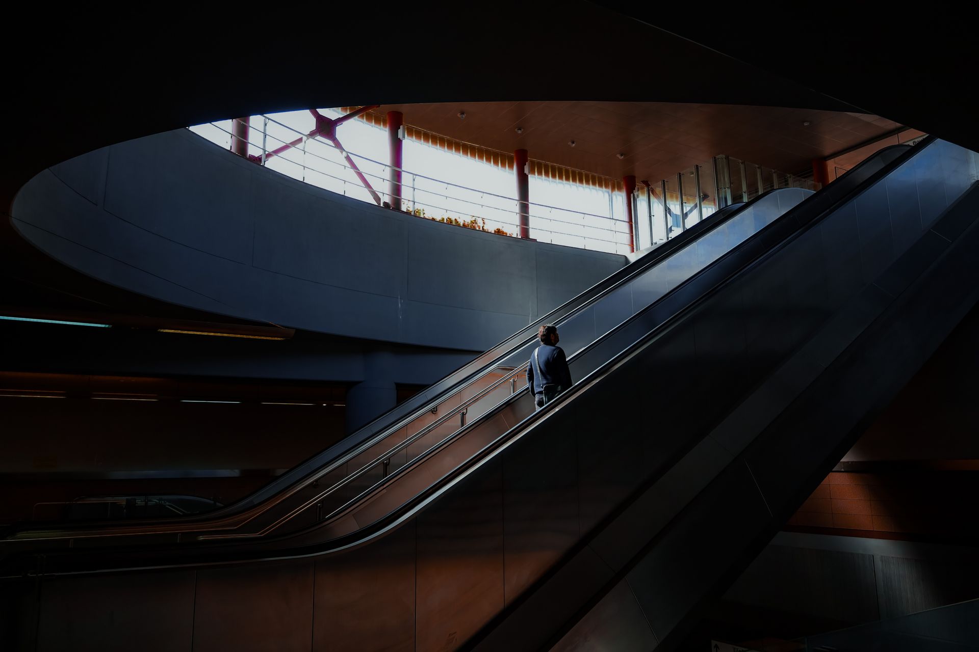 Man going up an escalator in a train station with light shining down on him in an empty building