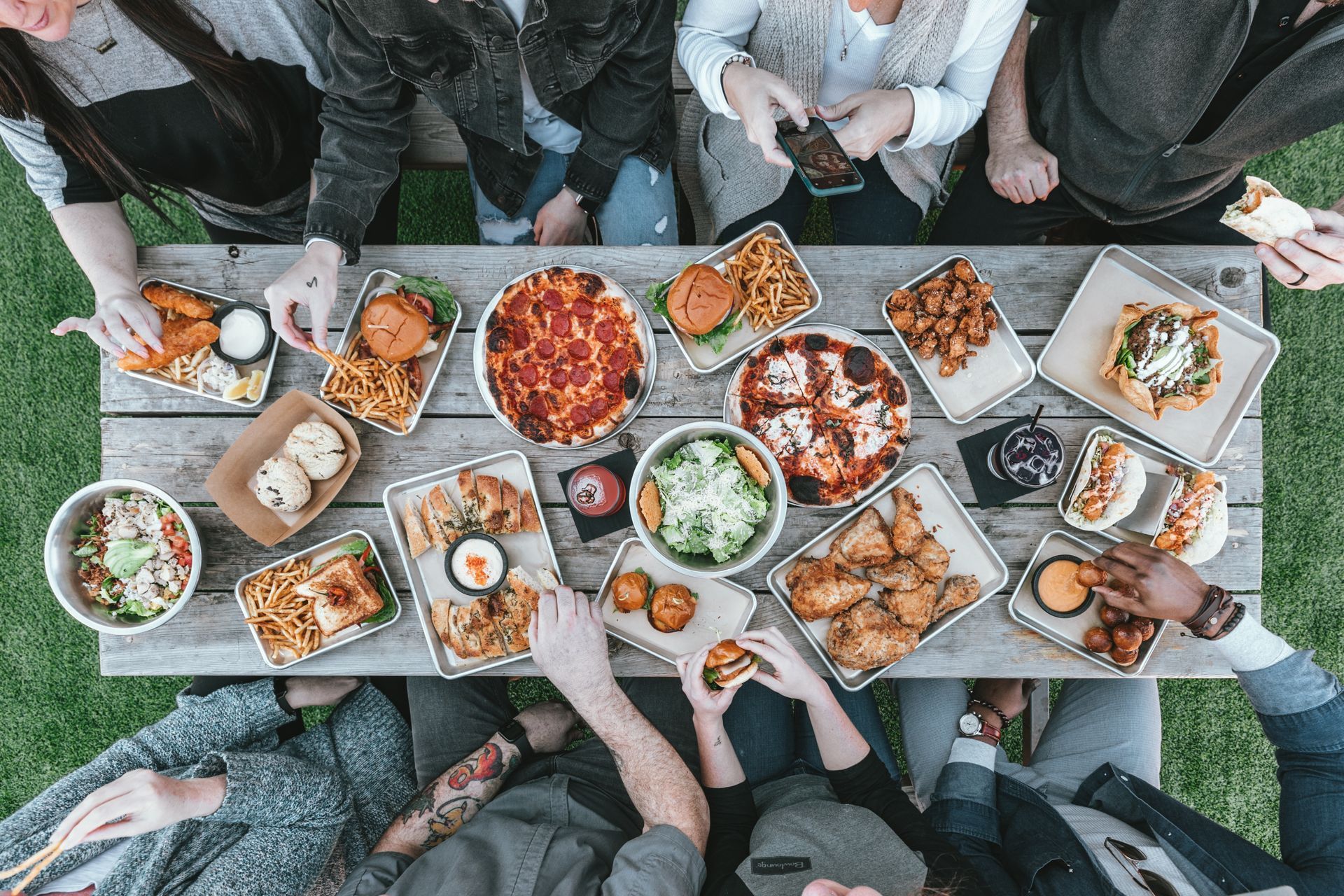 Thanksgiving meal on a picnic table with food and people sitting around it. 