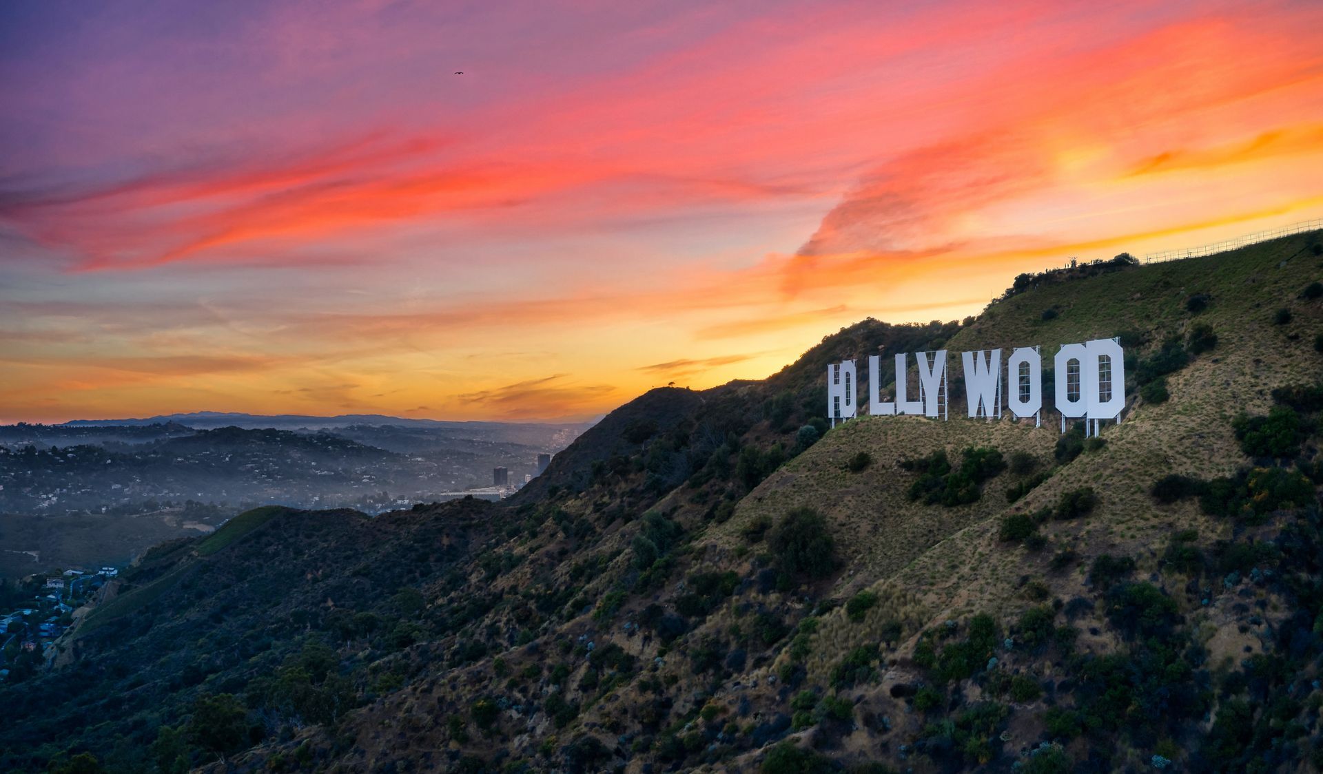 the mountain with the Hollywood sign with a beautiful sunset of pink, purple and gold clouds