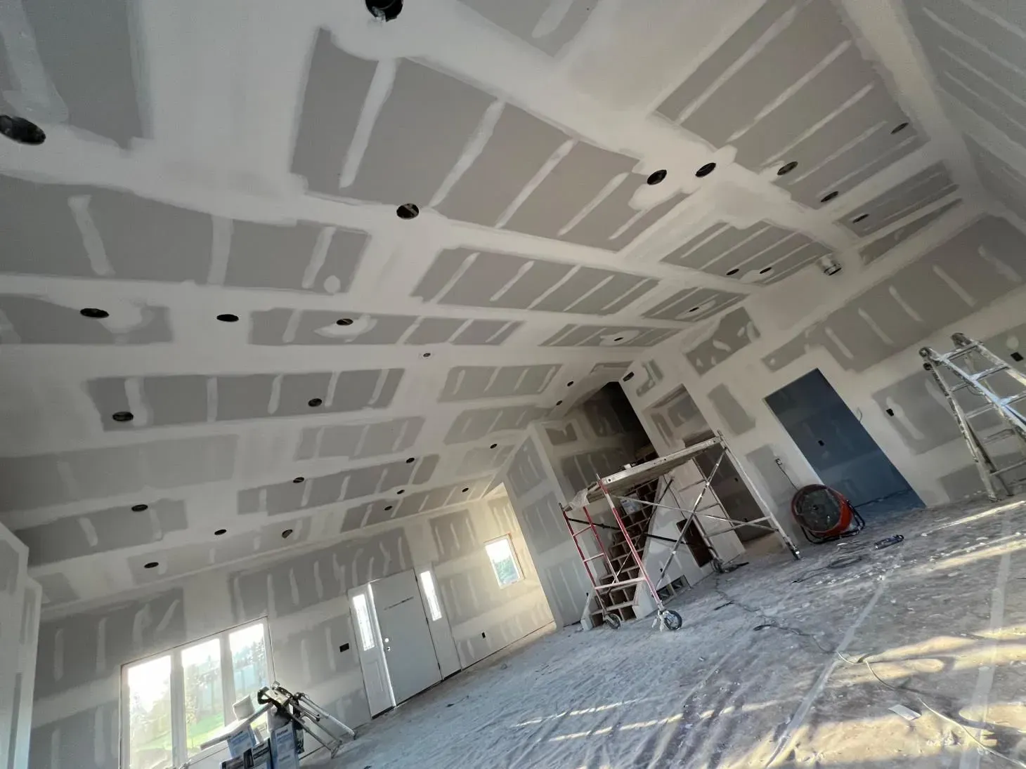Interior construction: drywall installed on ceiling and walls, with recessed lighting openings. Scaffolding visible.