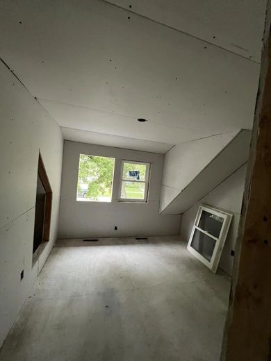 Interior view of a room under construction with drywall and unfinished concrete floor, and two windows.