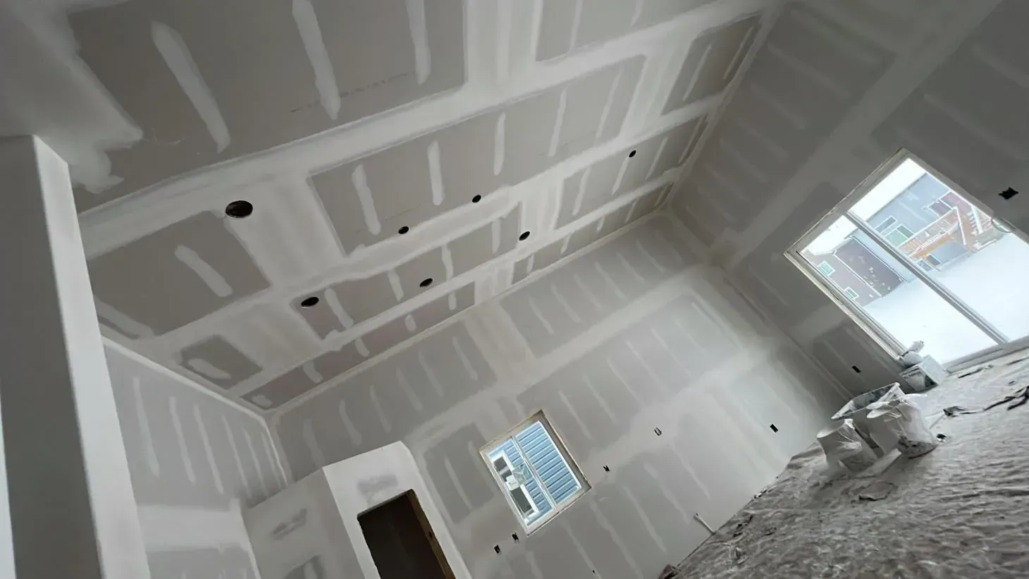 Interior room under construction, with drywall on walls and ceiling, window visible.