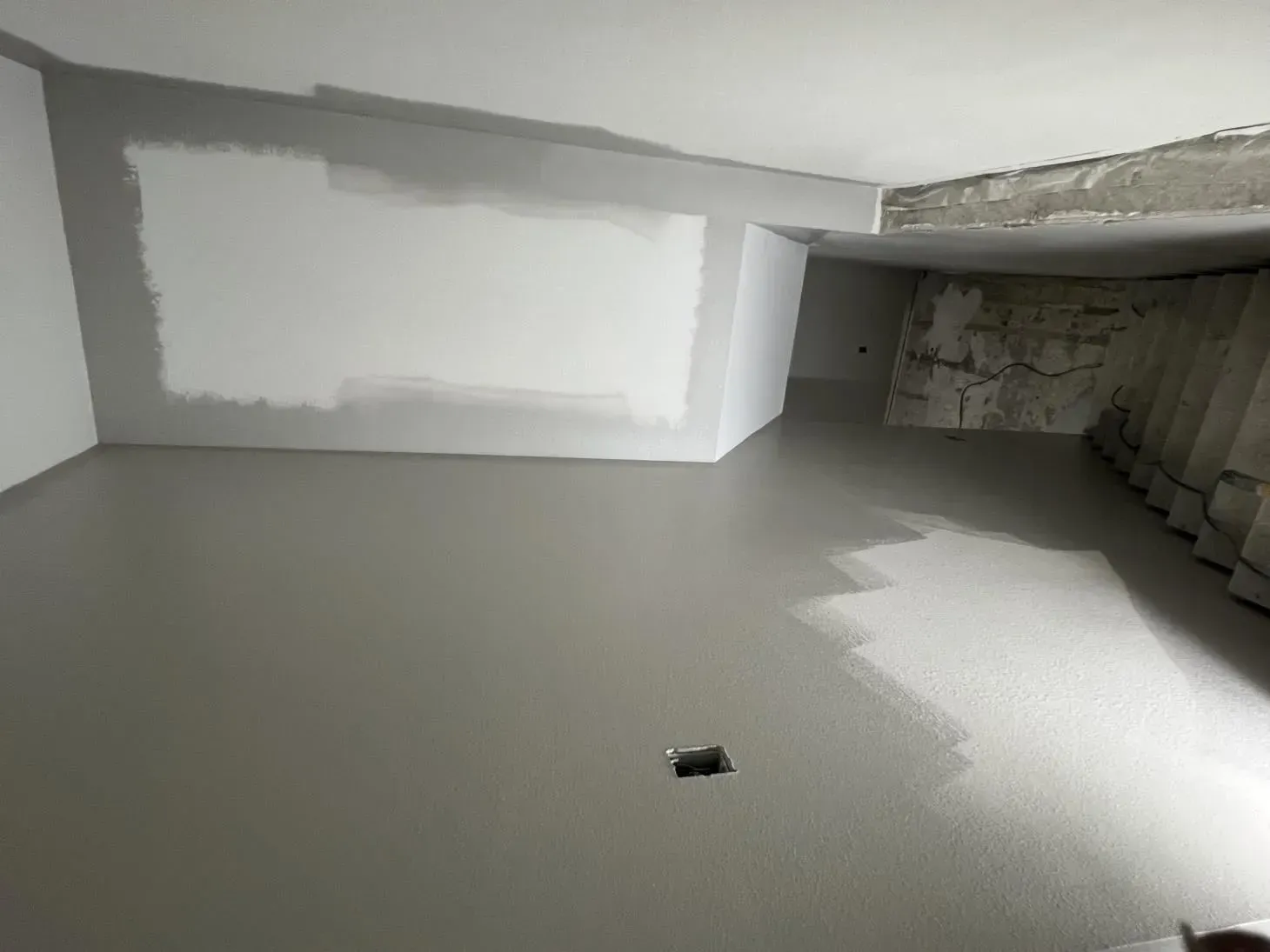 Newly finished room with gray concrete floor, white walls partially painted, and unfinished stairs.