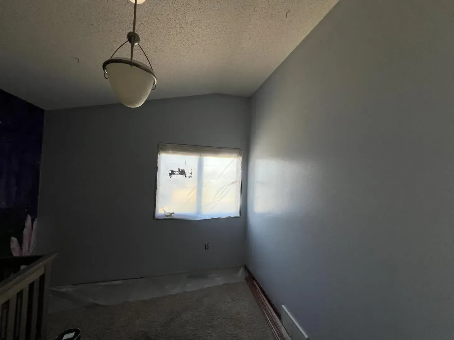 Empty room with gray walls, window covered in plastic, and a hanging light fixture.