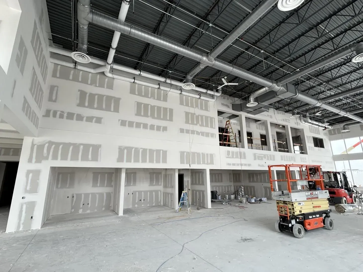 Interior construction site with drywall on walls and ceiling; exposed ventilation, lift, and equipment.