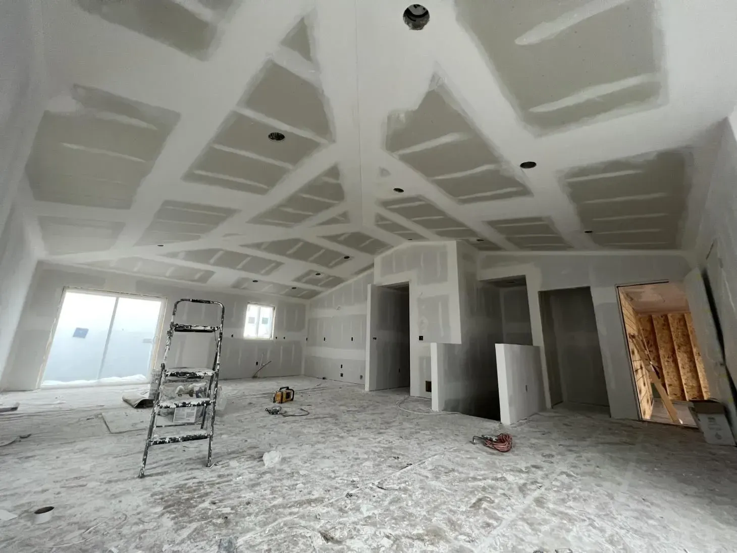 Interior of a room under construction with drywall on the ceiling and walls; ladder present.