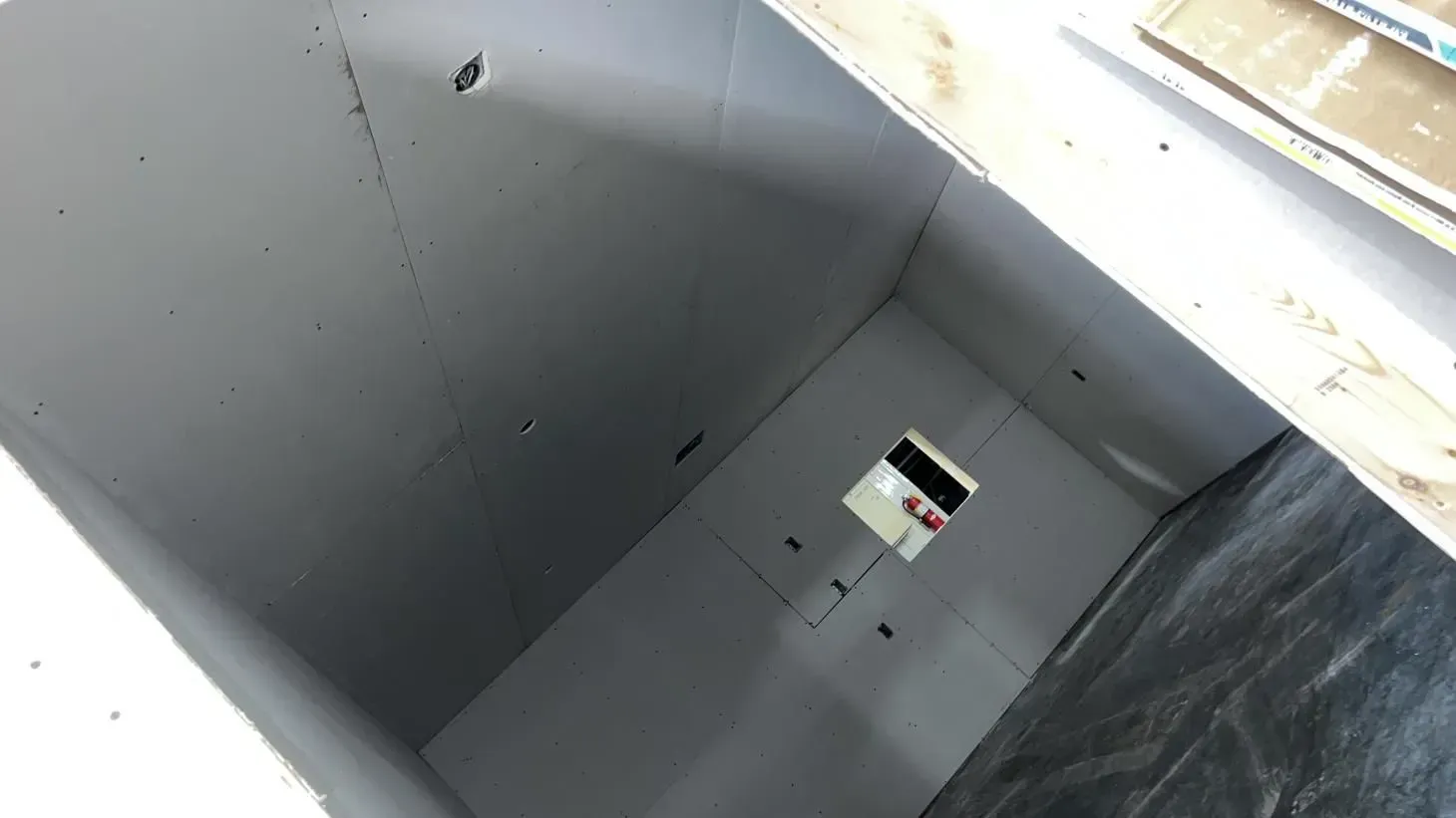 Interior view of a rectangular room under construction; white walls and ceiling, partially finished with a dark wall.