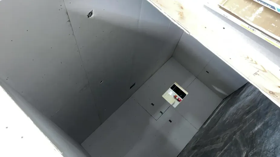 Interior of a room under construction with white walls, a small opening, and dark wall paneling.