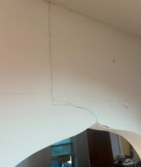 White wall with long crack, spanning from ceiling down towards arched opening.