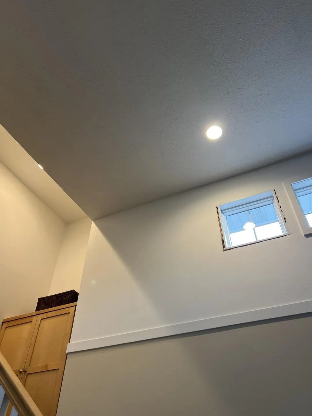 Interior view of a staircase, with a wall and window, and a recessed ceiling light.