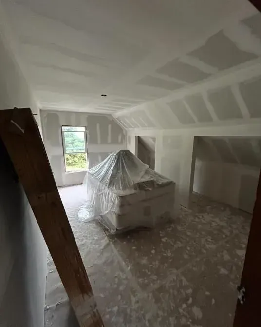 Interior room under construction with covered object, drywall, and unfinished surfaces.