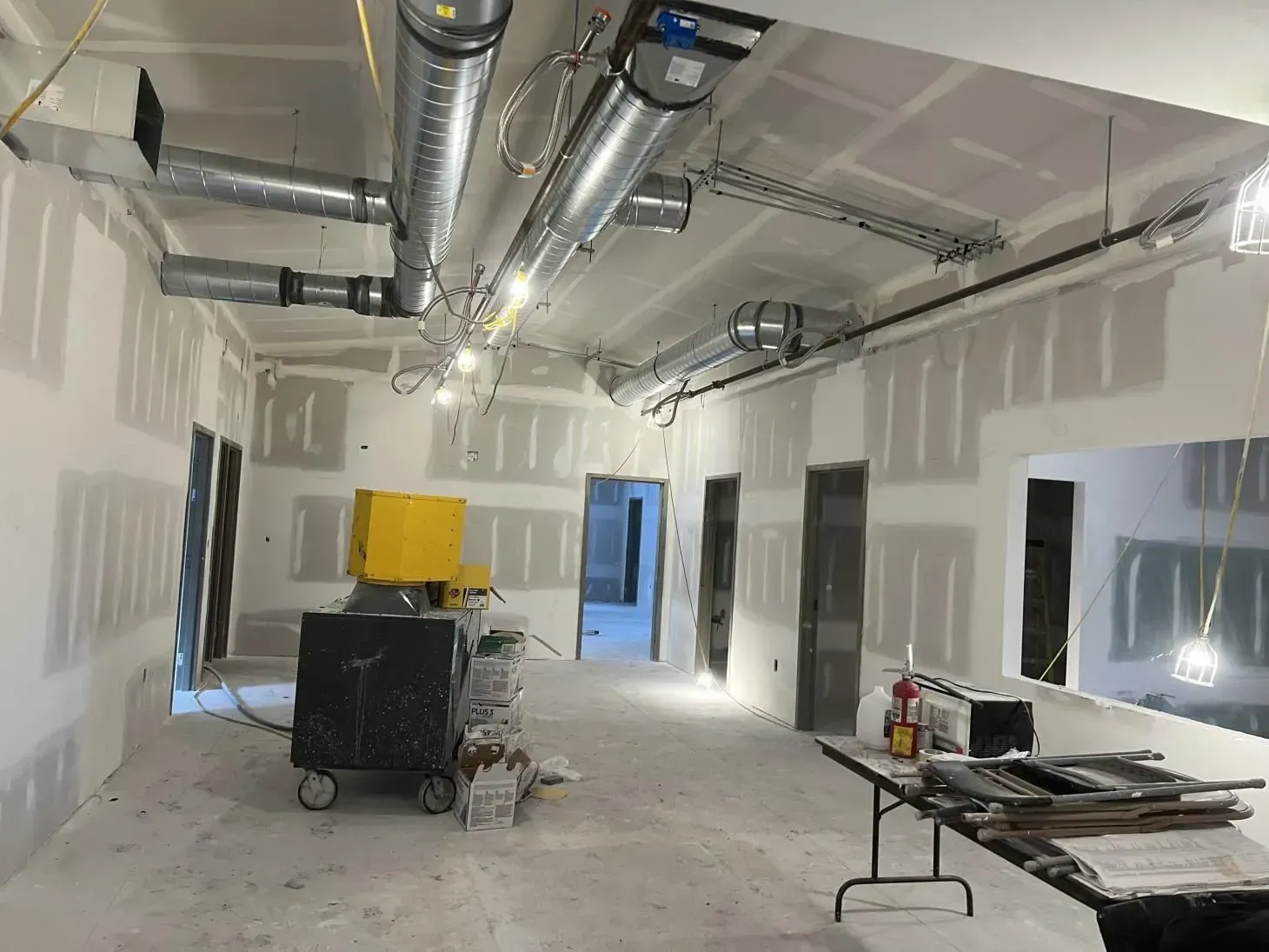 Interior view of a room under construction with exposed ductwork, drywall walls, and doorways.
