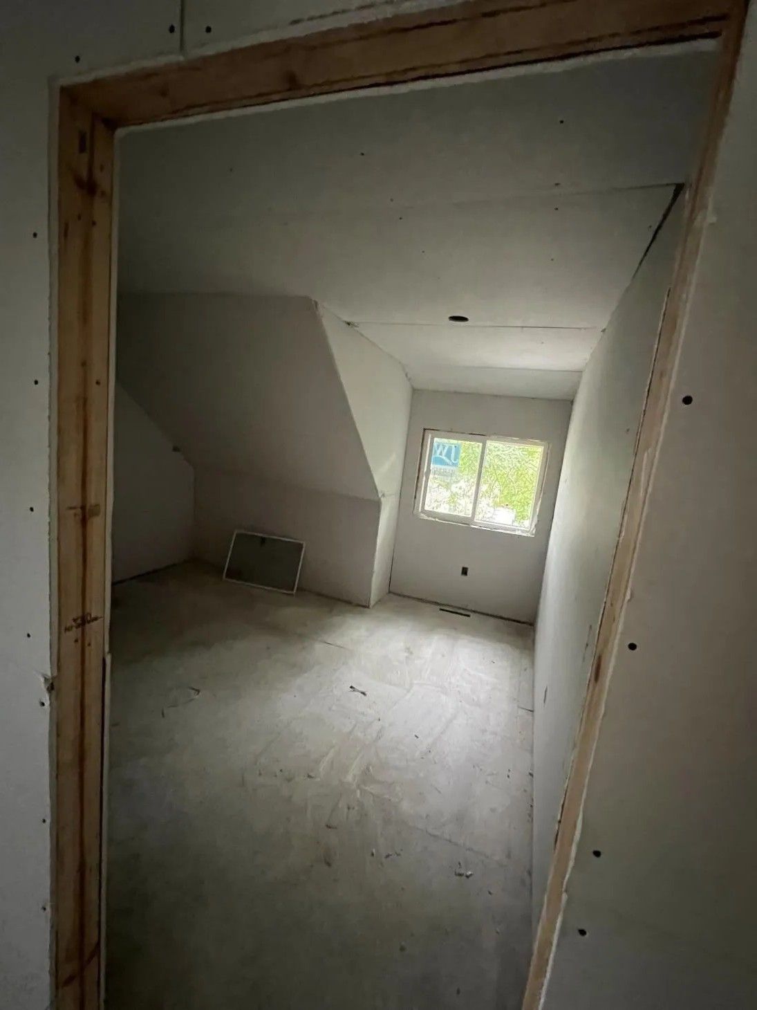 Room under construction, drywall, doorway frame, window, concrete floor, white walls.