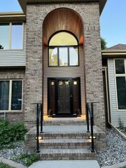 Brick home entrance with arched entryway, black door, and steps with handrails.