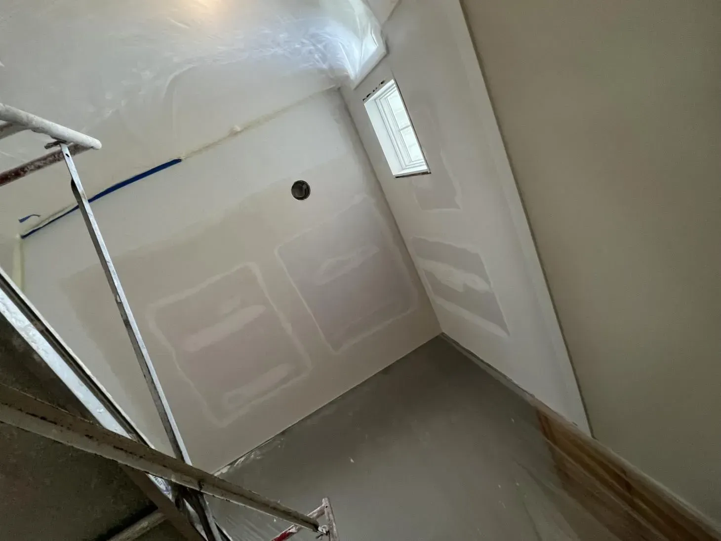Interior of a room under construction, with drywall and unfinished surfaces. Scaffolding is visible.