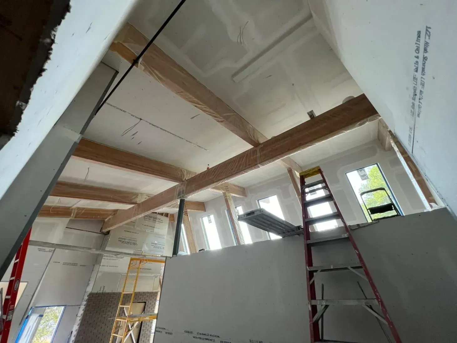 Interior under construction. Exposed wooden beams and drywall, ladder present.