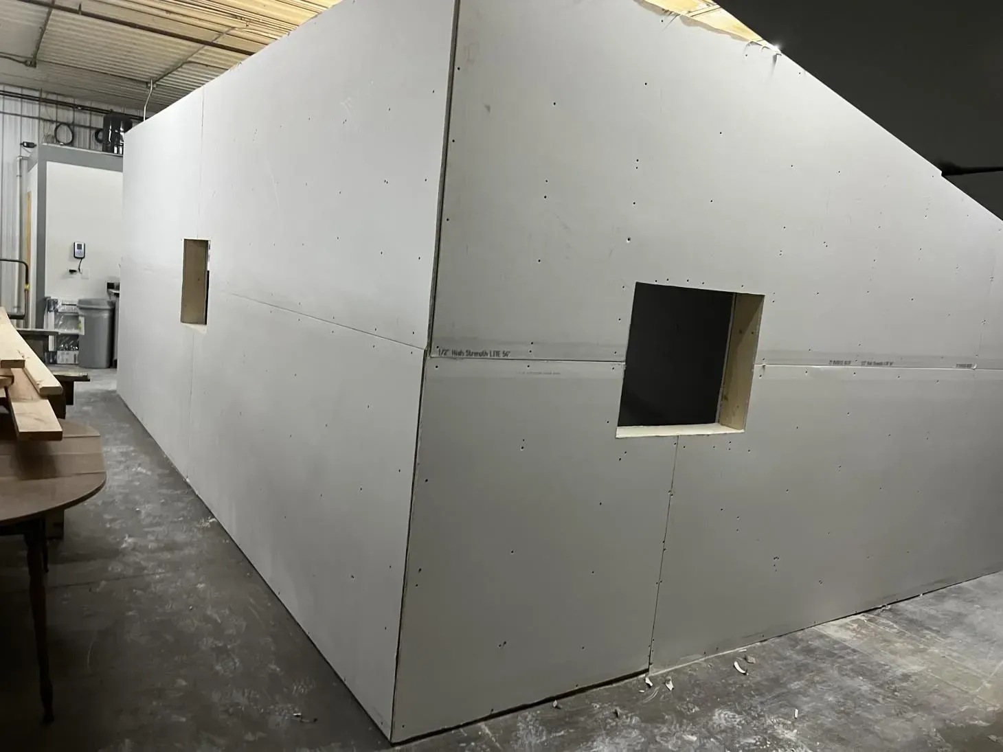 Large, white, unfinished drywall structure with two square openings, in an industrial setting.