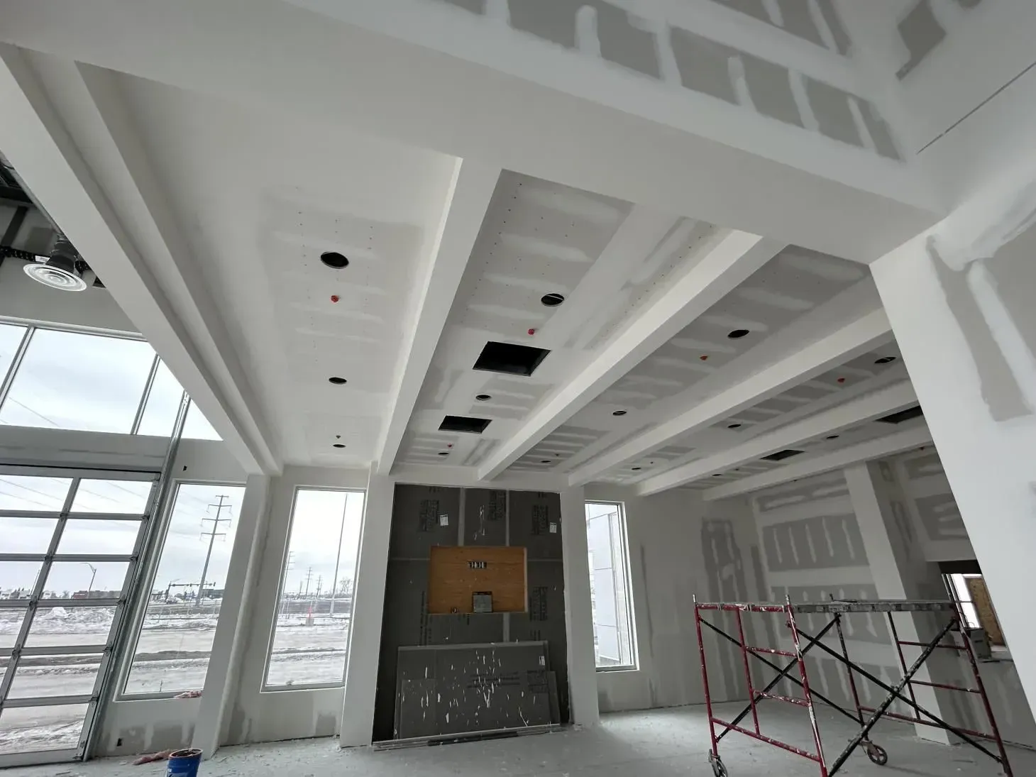 Interior construction of a building with white walls, ceiling beams, and exposed drywall.