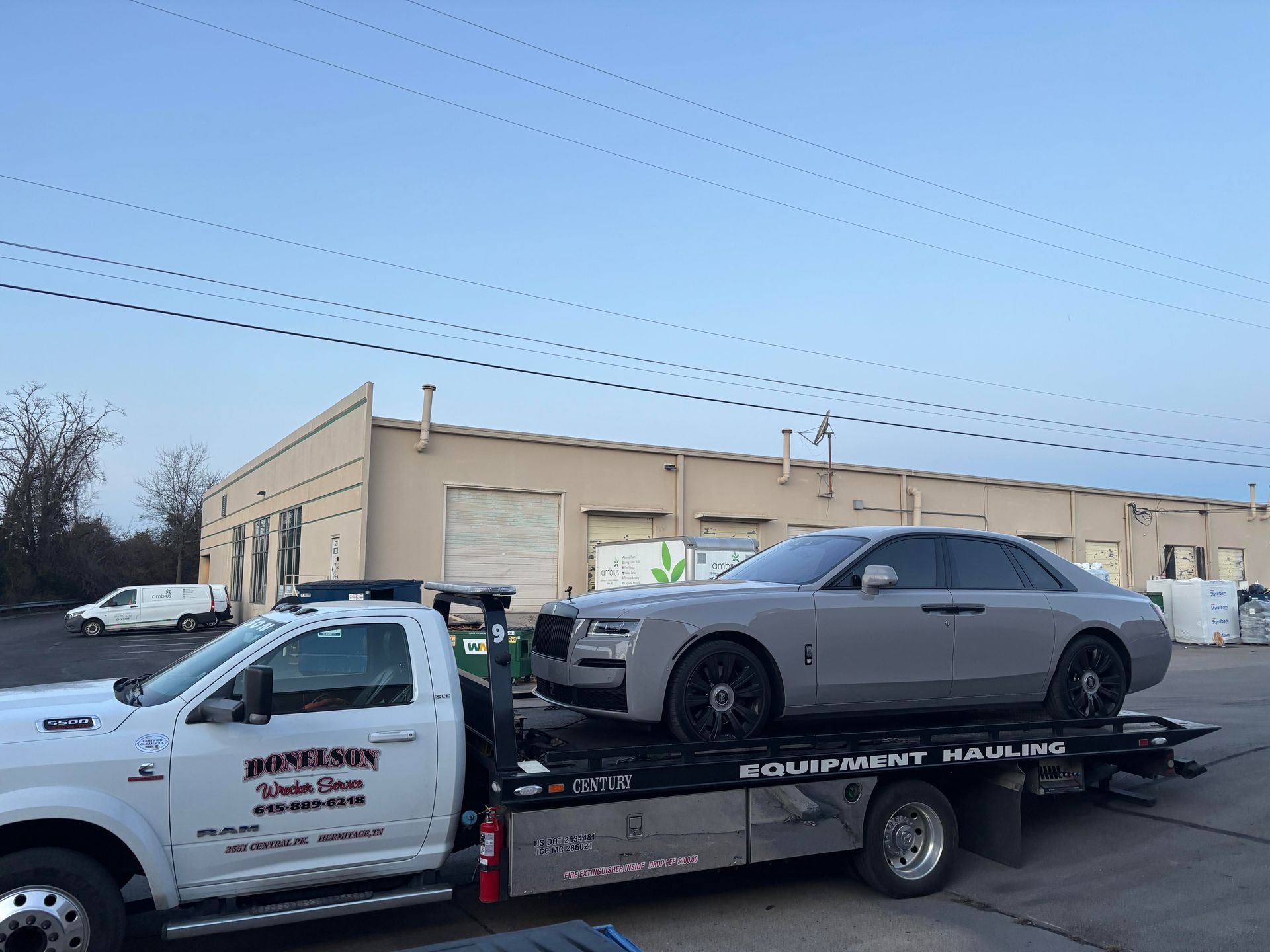 A grey Rolls Royce sedan on a flatbed tow truck in front of a building.