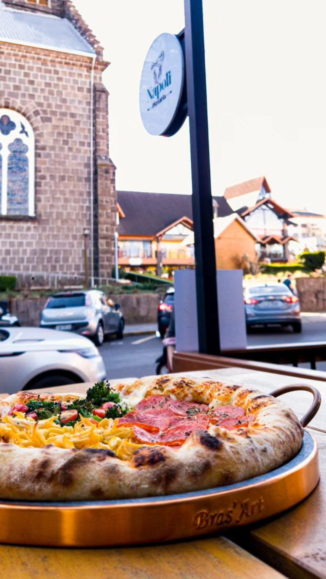Uma pizza está em uma bandeja sobre uma mesa em frente a uma igreja.
