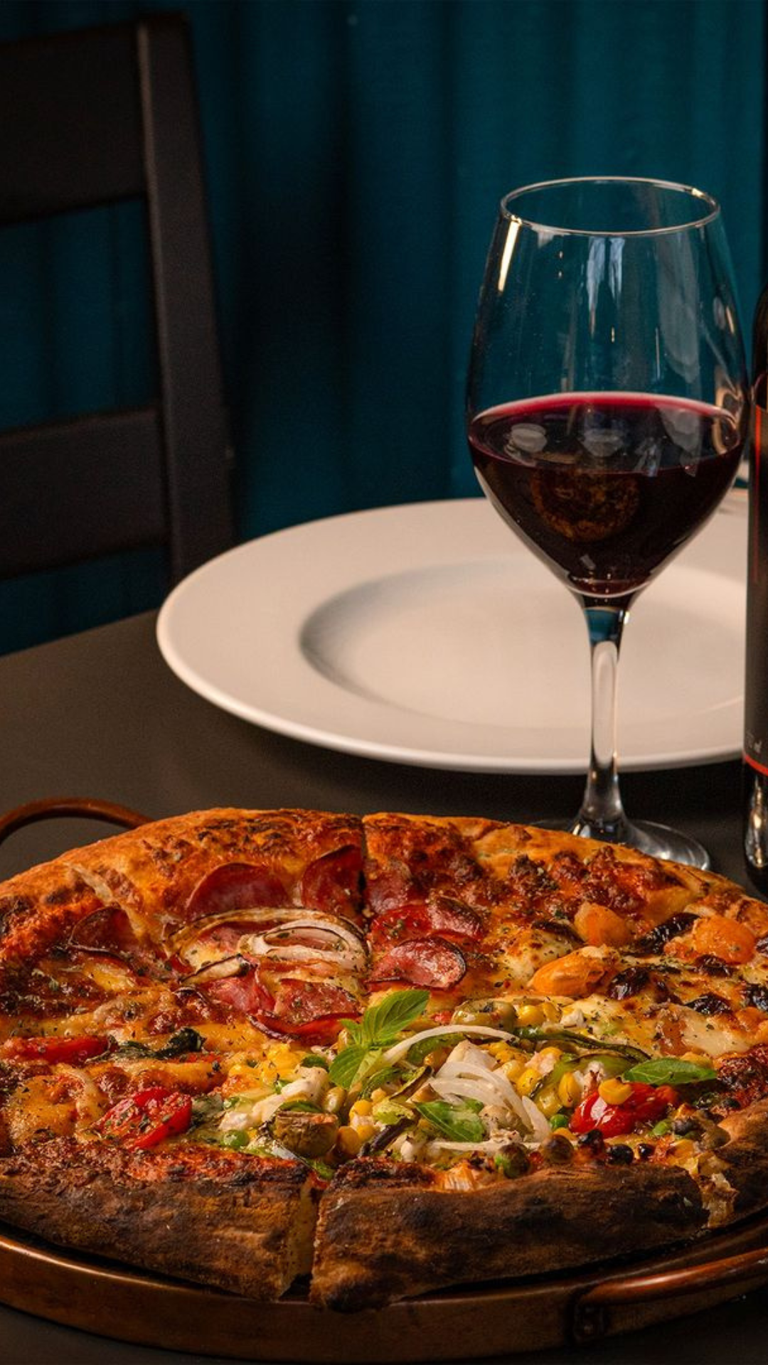 Uma pizza e uma taça de vinho estão sobre uma mesa.