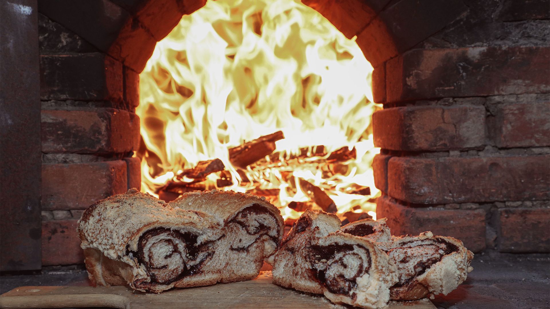 Duas fatias de pão estão sobre uma tábua em frente a um forno de tijolos.