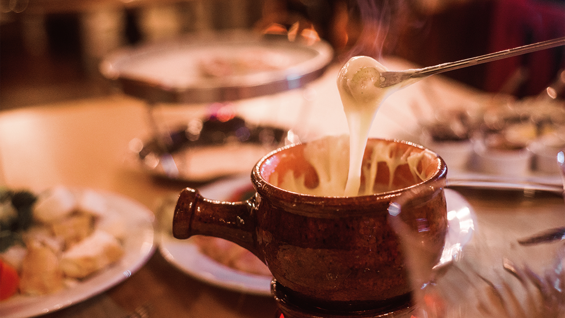 Uma pessoa está mergulhando um pedaço de queijo em uma tigela de fondue.