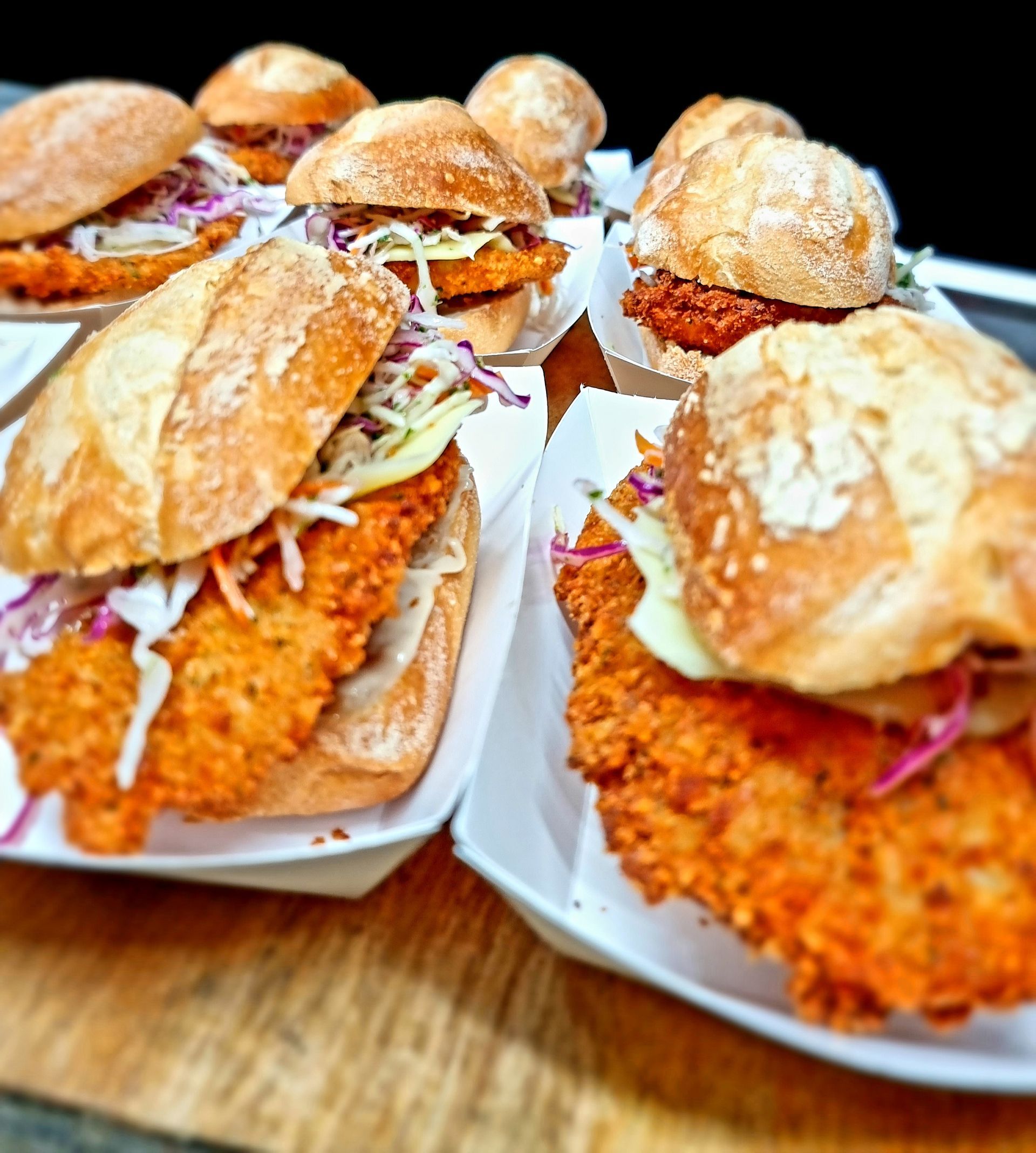 A bunch of fried chicken sandwiches are sitting on a wooden table.