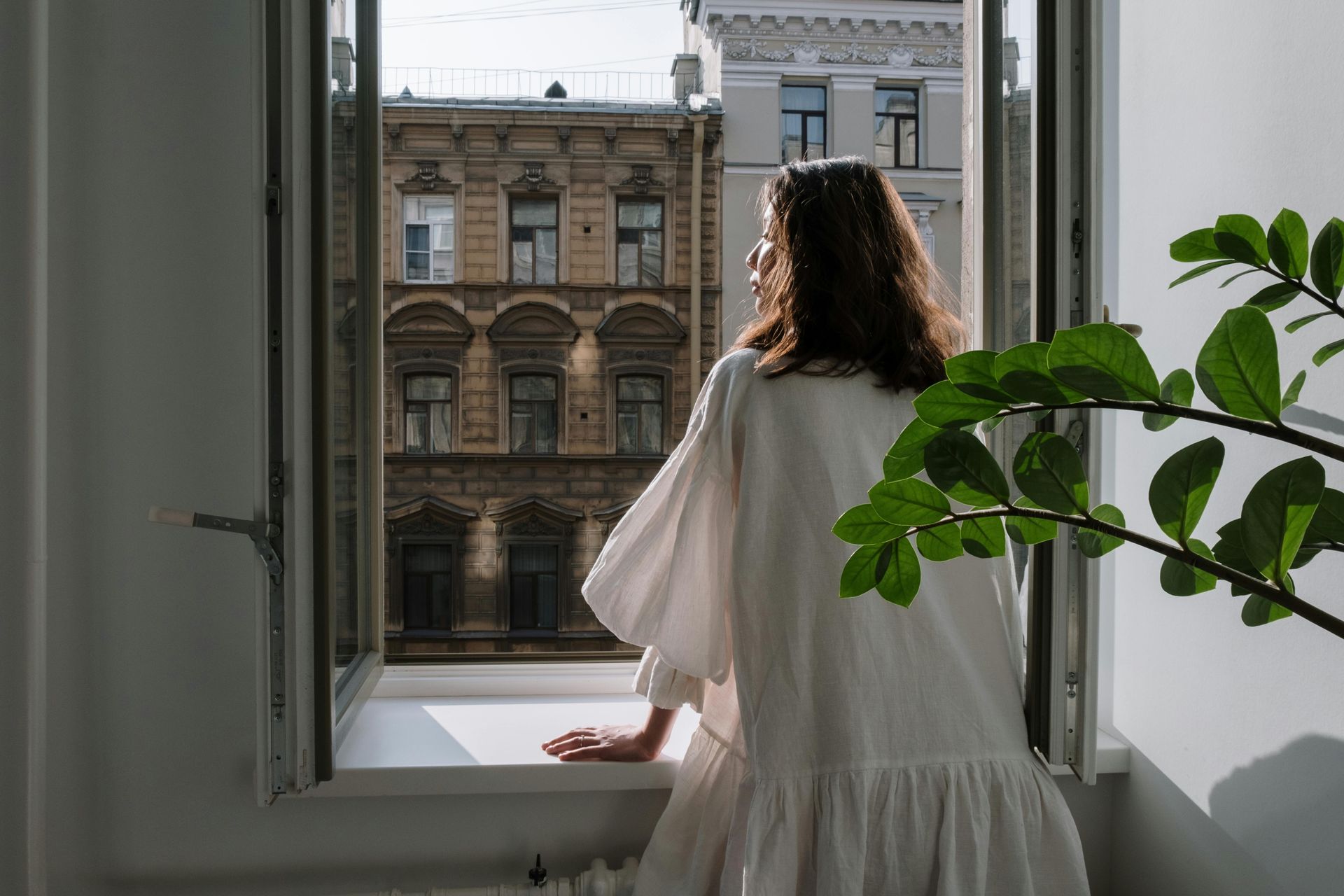 Woman standing by open window in quiet reflection symbolizing emotional healing and personal growth